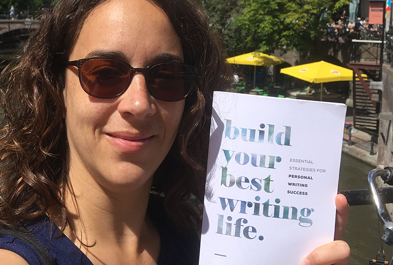 Heleen met zonnebril aan de gracht met het boek 'Build your best writing life'